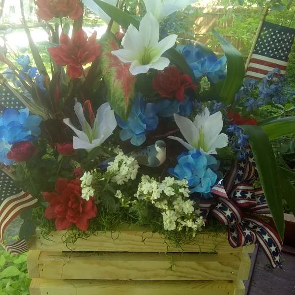 Red, white, and blue floral arrangement in a wooden crate with ribbon