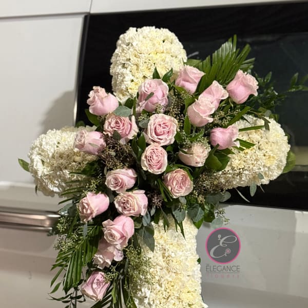 Pink roses and white floral spray arranged on a standing cross
