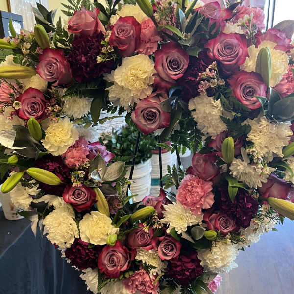 Heart-shaped floral wreath with pink roses and white carnations on an easel