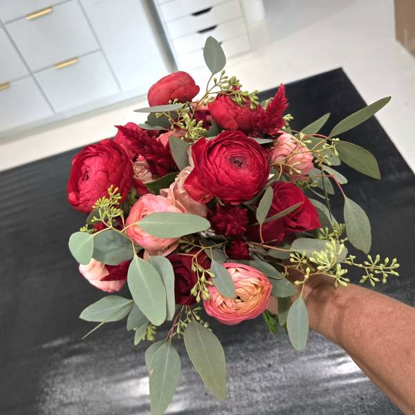 Handheld bouquet of red and pink flowers with eucalyptus foliage