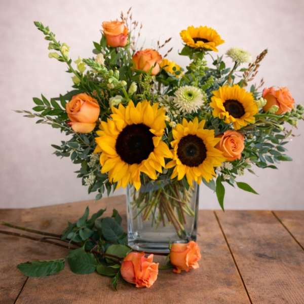 Sunflowers and orange roses arranged in a clear glass vase