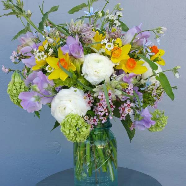 Mixed bouquet of yellow, purple, and white flowers in a glass jar vase