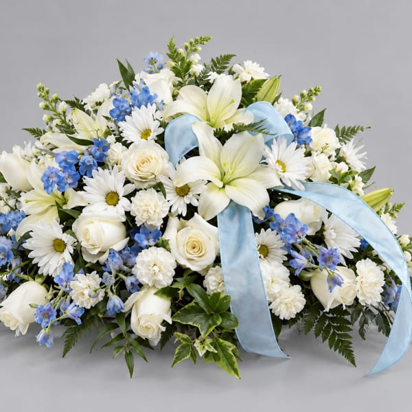 White lilies, roses, and blue flowers arranged with a light blue ribbon