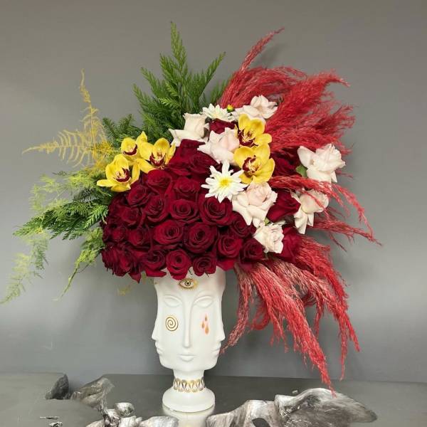 Large floral arrangement in a white sculptural vase with red, yellow, and white blooms