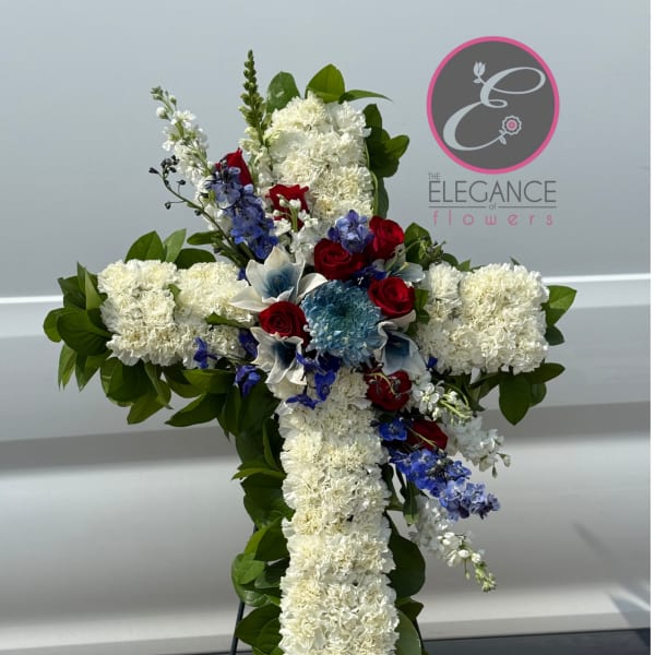 Cross-shaped floral tribute with white carnations, red roses, and blue accents