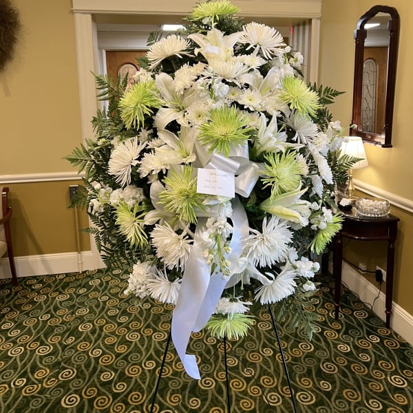 Large white funeral wreath with lilies and green spider mums on a stand