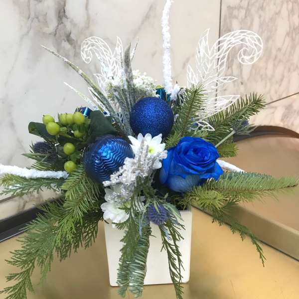 Blue rose arrangement with pine branches and ornaments in a white vase