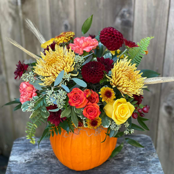 Mixed bouquet in an orange pumpkin container with yellow, red, and pink blooms