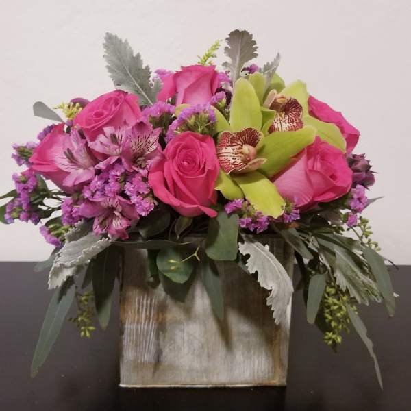 Pink roses and orchids in a square vase with silver foliage