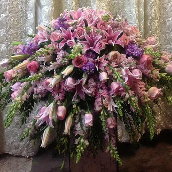 Large cascading arrangement of pink lilies and roses with purple accents on a pedestal stand