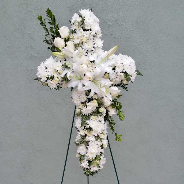 Standing cross-shaped spray of white lilies, roses, and mums on an easel