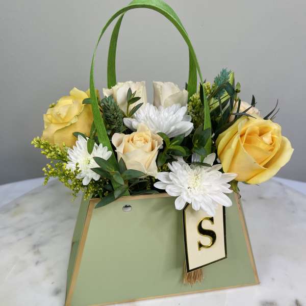 Yellow and white roses with white daisies in a green gift bag