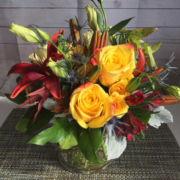 Mixed bouquet of yellow roses, red lilies, and buds in a glass vase