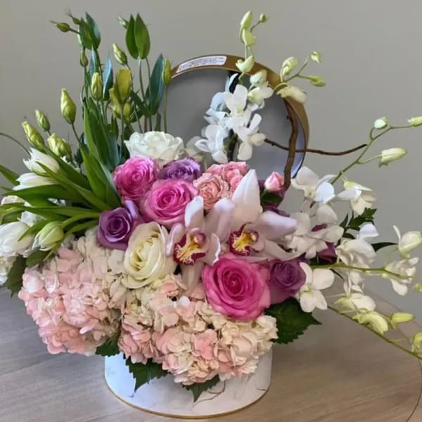 Round box arrangement of pink roses, orchids, tulips, hydrangeas and white orchids with green buds
