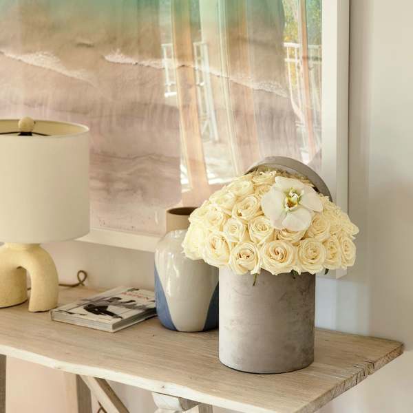 Cream rose arrangement in a gray cylindrical vase with a white orchid bloom