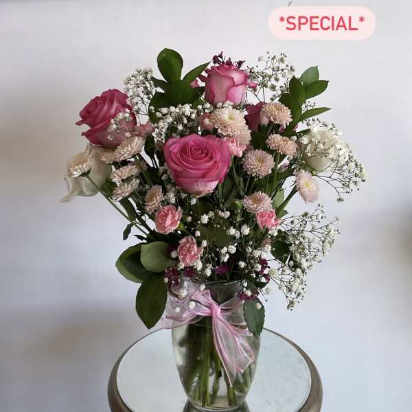 Pink roses and small white flowers in a clear glass vase with a pink ribbon