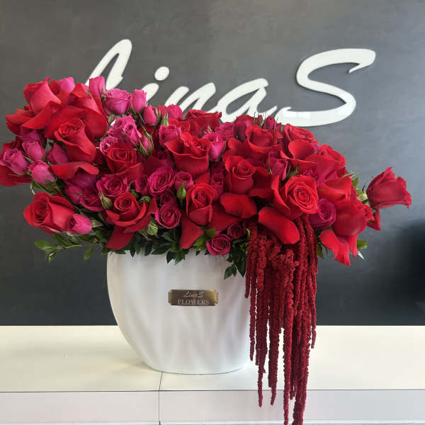 Large red and pink rose arrangement in a white vase