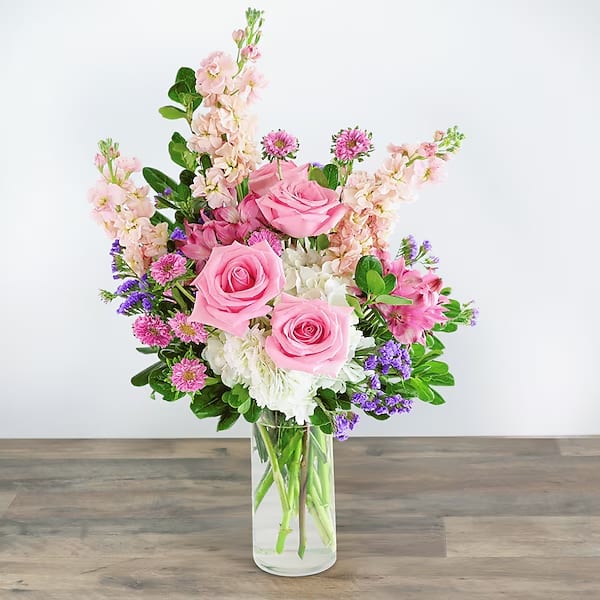 Pink roses and mixed flowers arranged in a clear glass vase