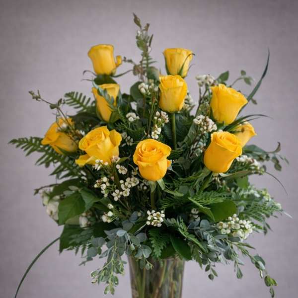 Yellow roses arranged in a clear glass vase with greenery