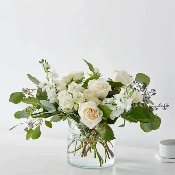 Low arrangement of white and cream roses in a clear glass vase.