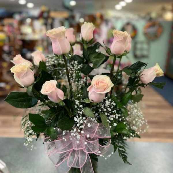 Pink roses arranged in a glass vase with a pink ribbon bow