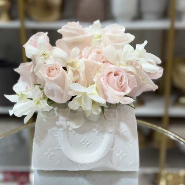 Blush pink roses and white orchids in a white gift bag