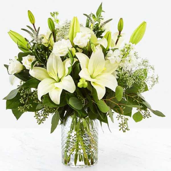 Arrangement of white lilies and white blooms in a clear patterned glass vase