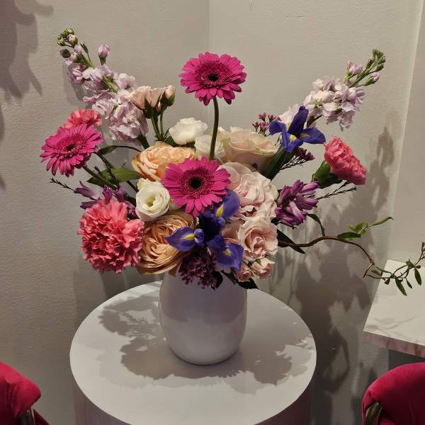 Mixed bouquet of pink, peach, white, and purple flowers in a white vase