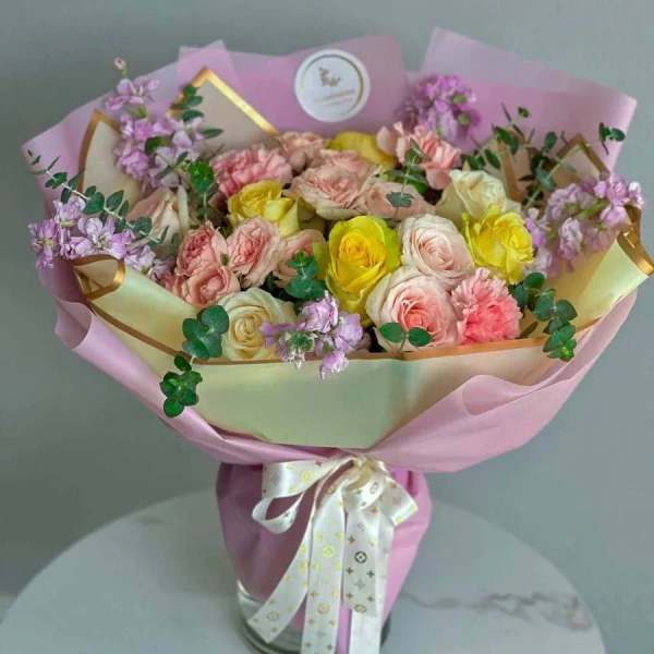 Bouquet of pink, yellow, and white roses wrapped in pink paper
