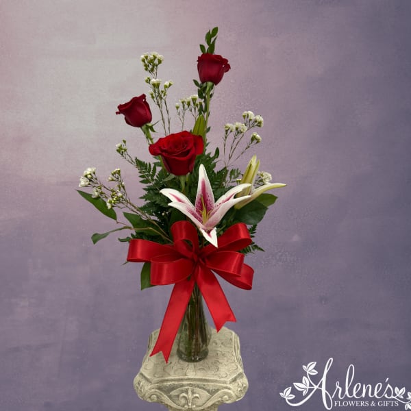 Red roses and a lily in a glass vase with a red ribbon