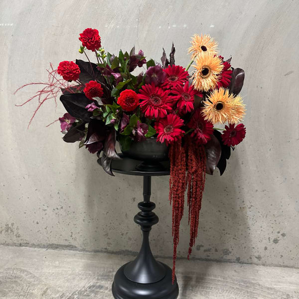 Red and orange floral arrangement in a black pedestal vase