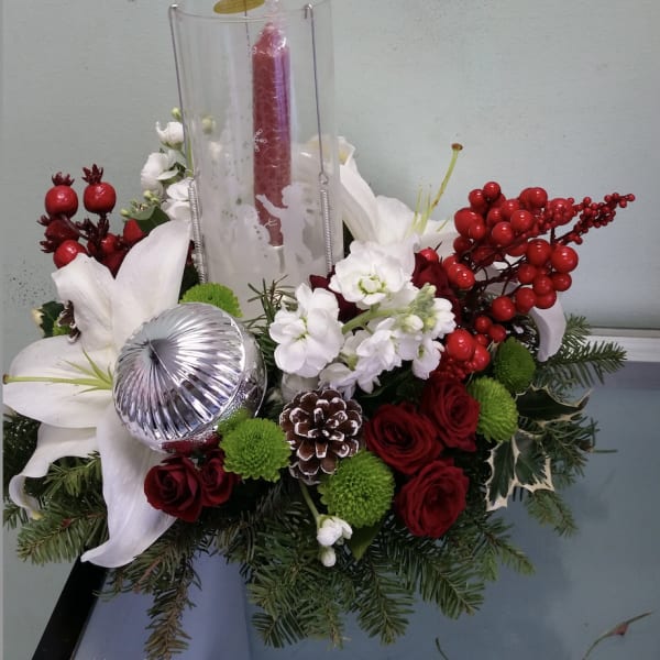 Holiday floral centerpiece with white lilies, red roses, and a tall red candle