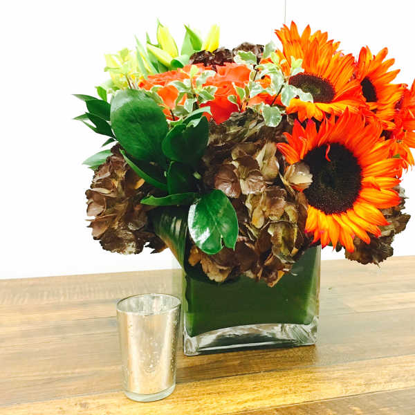 Orange sunflowers and mixed blooms in a square glass vase