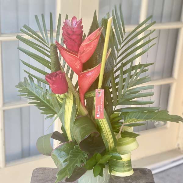 Tropical arrangement with red heliconia and palm leaves in a mint vase