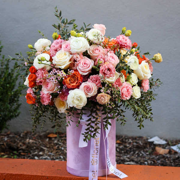 Large bouquet of pink, white, and orange roses in a lavender hat box