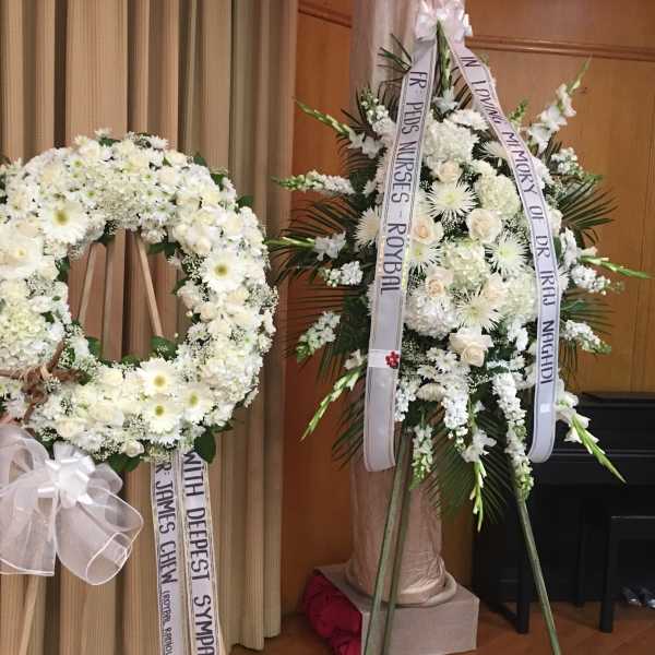 Two white funeral flower wreaths with condolence ribbons on stands