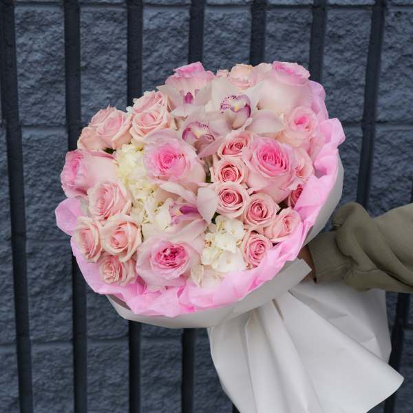 Bouquet of pink roses and pale orchids wrapped in white paper