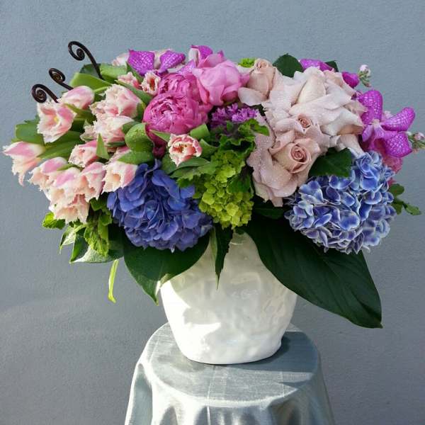 Mixed pink, purple, and blue flowers arranged in a white vase