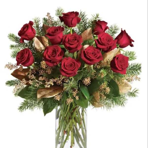 Red roses arranged in a clear glass vase with evergreen accents