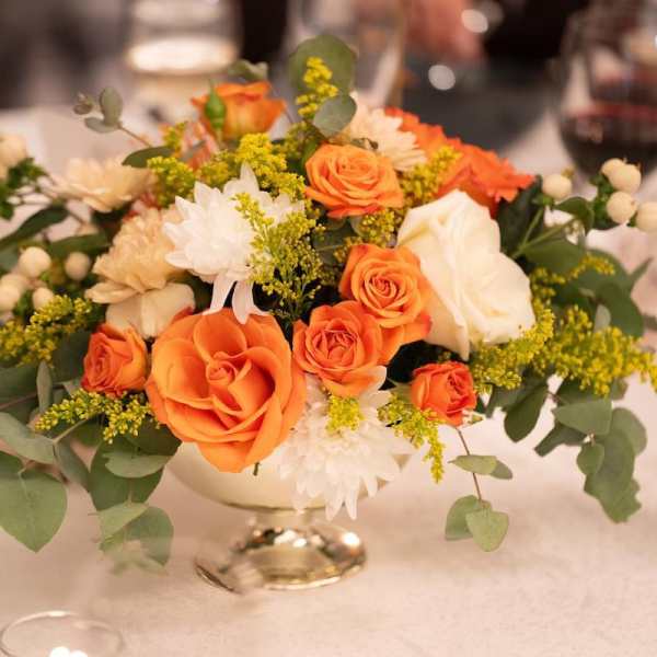 Orange and white rose centerpiece in a low silver vase