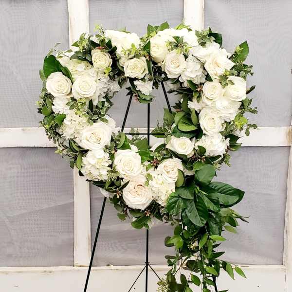 Heart-shaped white rose wreath on a black stand with trailing greenery
