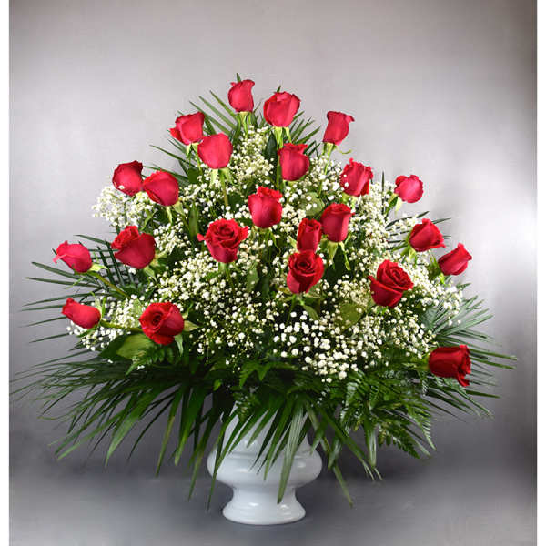 Red roses arranged in a white pedestal vase with baby's breath