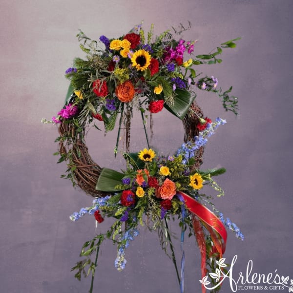 Large double grapevine wreath with bright mixed flowers and ribbons on a stand