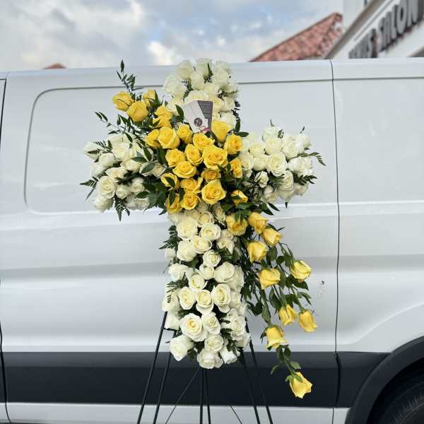 Cross-shaped floral tribute of white and yellow roses on a stand