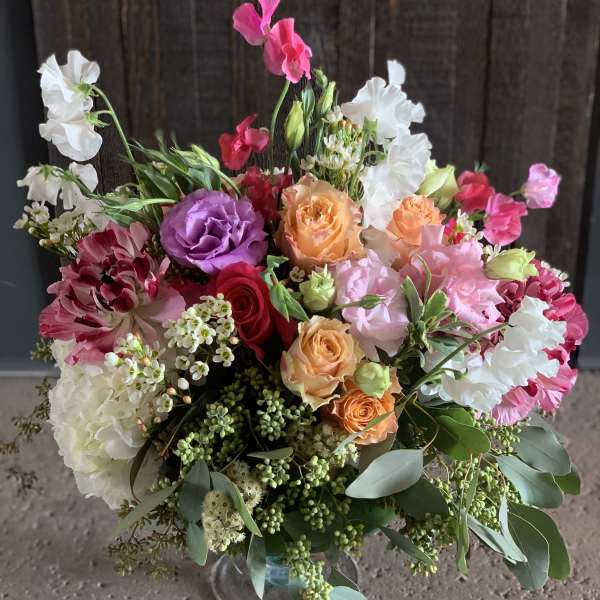 Mixed bouquet of roses, lisianthus, and sweet peas in a glass vase