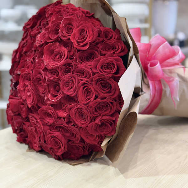 Large bouquet of red roses wrapped in brown paper with a pink ribbon