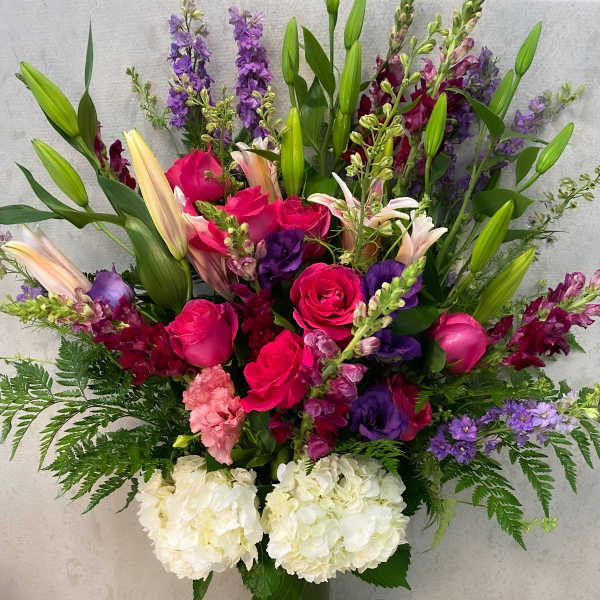 Tall bouquet of pink roses, lilies, and purple flowers in a glass vase