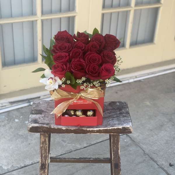 Red rose arrangement in a red gift box with chocolates and a gold ribbon