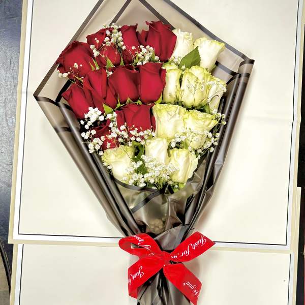 Bouquet of red and white roses wrapped in dark paper with a red ribbon