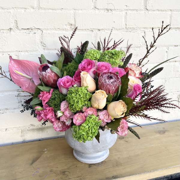 Pink and cream floral arrangement in a white pedestal vase
